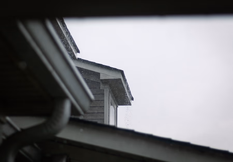 A house roofline in heavy rain, with water shedding off a section of eave that has no gutter beneath it