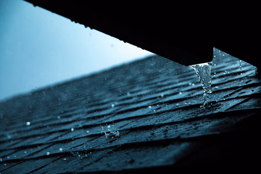 Close view of rainwater pouring off the edge of a shingle roof in a single concentrated stream